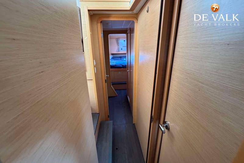 Een gang met houten wanden en een donkere vloer leidt naar een slaapkamer met een bed en een raam.