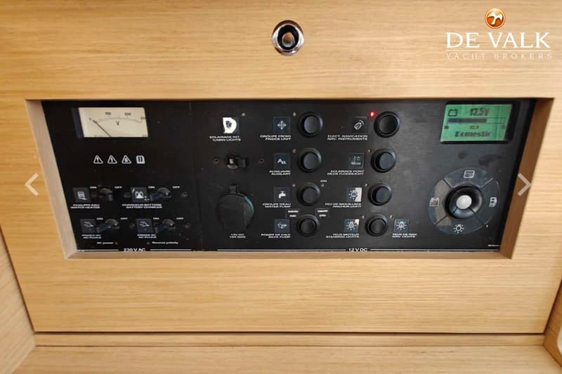 Een zwart bedieningspaneel met diverse schakelaars, knoppen, een voltmeter en een digitaal display, gemonteerd in licht hout.