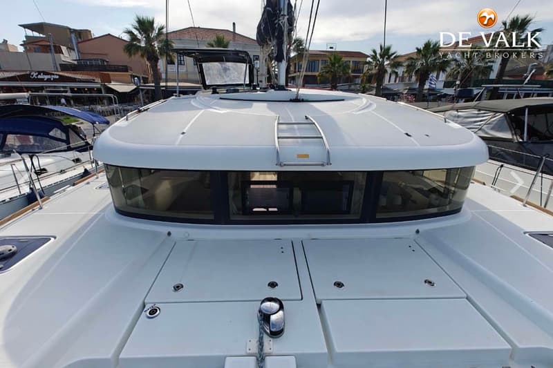 Een witte boot met een kajuit en een mast, liggend in een haven met gebouwen en palmbomen op de achtergrond. — Lagoon 39