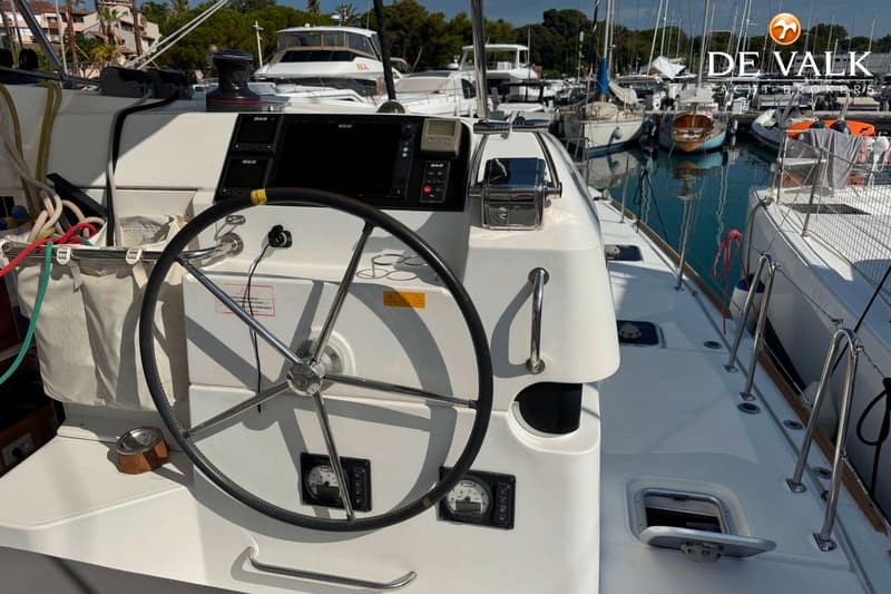 Een stuurwiel met instrumentenpanelen en een plotter op een boot, met andere boten in een haven op de achtergrond.