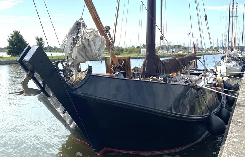 Een donkerblauwe zeilboot met een opgevouwen zeil en anker ligt aangemeerd aan een kade. — Schokker 14.00 M. One Off