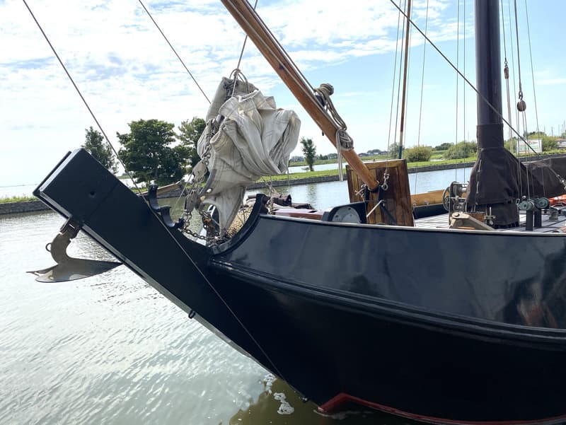 De boeg van een donkerblauwe zeilboot met een anker en opgevouwen zeil, liggend in het water. — Schokker 14.00 M. One Off