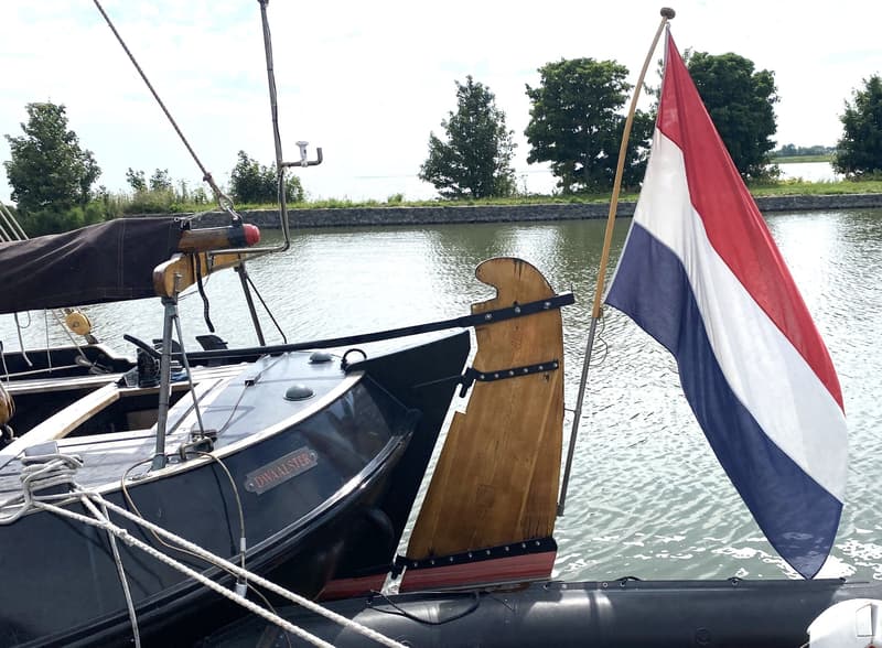 Een boot met de naam "DWAALSTER" ligt in het water, met een Nederlandse vlag aan de achtersteven. — Schokker 14.00 M. One Off