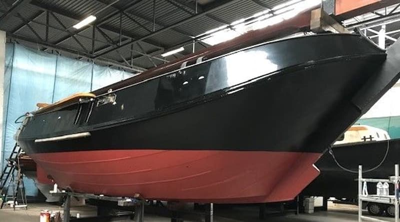 Een zwarte boot met een rode onderkant staat op bokken in een loods. — Schokker 14.00 M. One Off
