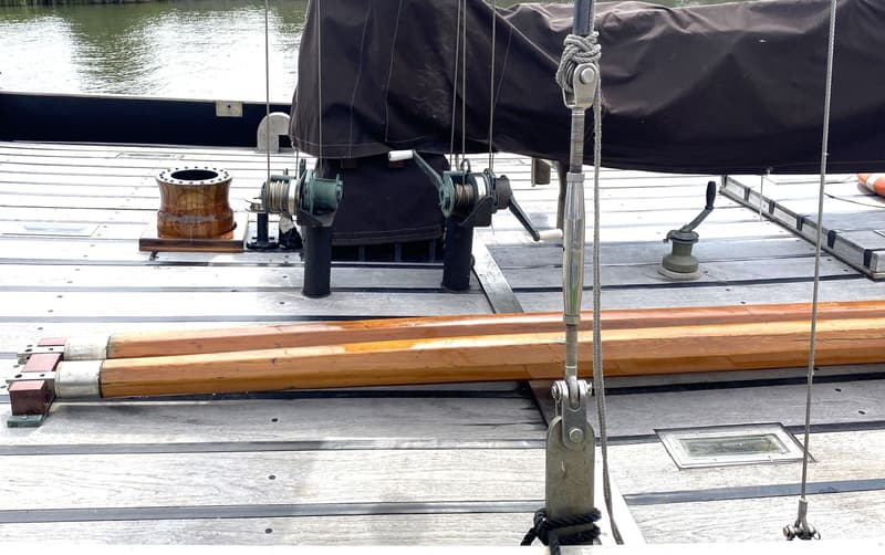 Een dek van een boot met houten planken, twee houten masten, lieren en een zwart zeil. — Schokker 14.00 M. One Off