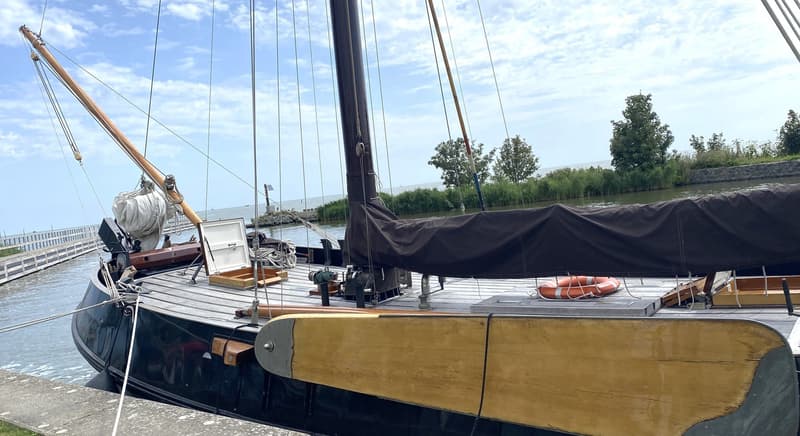 Een zeilboot met een zwart zeil en een houten giek ligt aangemeerd aan een kade. — Schokker 14.00 M. One Off