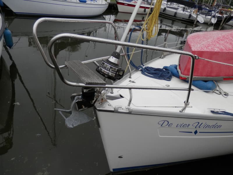 De boeg van een witte zeilboot met de naam "De vier Winden" is zichtbaar, inclusief anker, preekstoel en een Furlex…