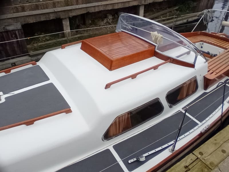 Een witte boot met houten details en donkere antislipmatten ligt aangemeerd aan een houten steiger. — Delphin 66