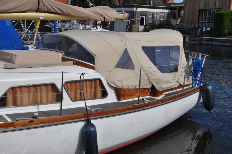 Een witte zeilboot met een beige buiskap en een beige huik ligt afgemeerd in het water. — Delphin 66