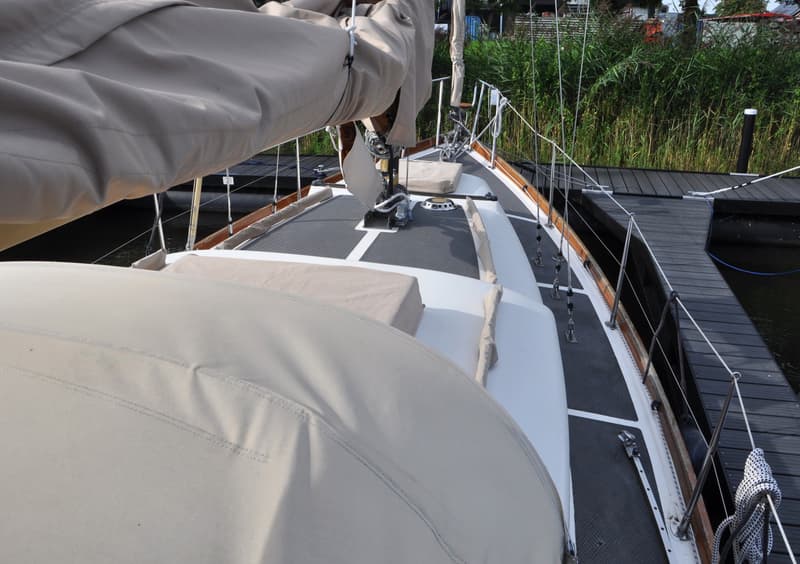 Een zeilboot ligt aangemeerd aan een donkere houten steiger, met riet langs de oever op de achtergrond. — Delphin 66