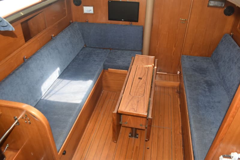 De foto toont het interieur van een boot met houten wanden en vloer, blauwe kussens en een tafel in het midden.