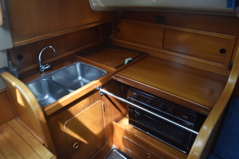 Een houten scheepskeuken met een dubbele roestvrijstalen spoelbak, een kraan en een ingebouwd fornuis met oven.