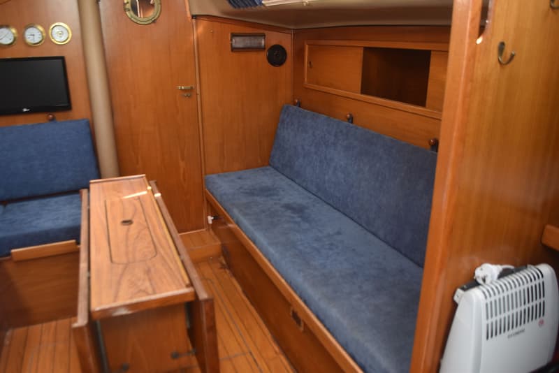 De foto toont het interieur van een boot met houten wanden, blauwe zitbanken, een tafel en een Hyundai kachel.