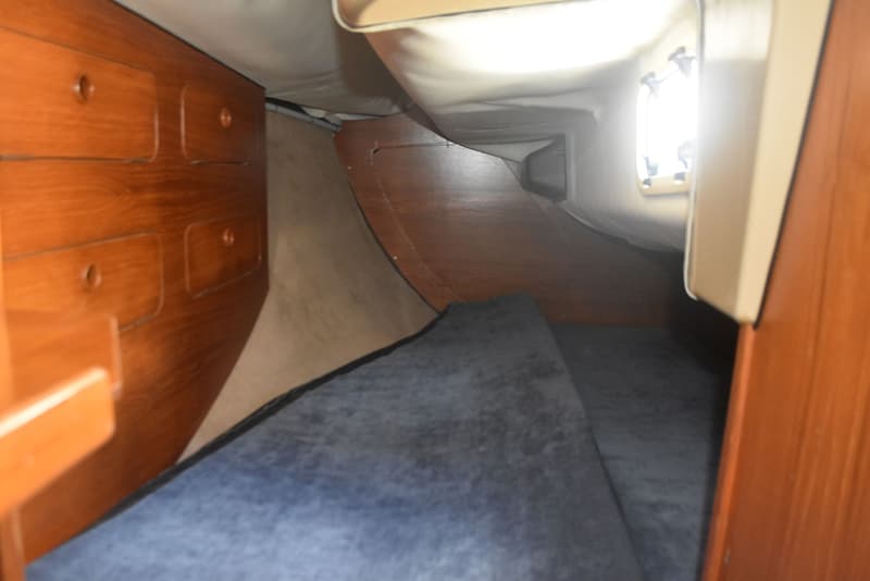 Een interieur van een boot met houten kasten, een blauw tapijt en een raam met fel licht. — Dehler Optima 101