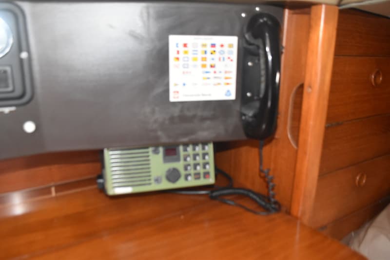 Een groene marifoon met een zwart telefoontoestel hangen aan een donker paneel boven een houten tafel.