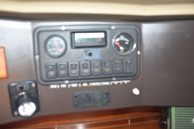 Een donkergrijs dashboard met meters, schakelaars en een display, met daaronder een houten paneel.