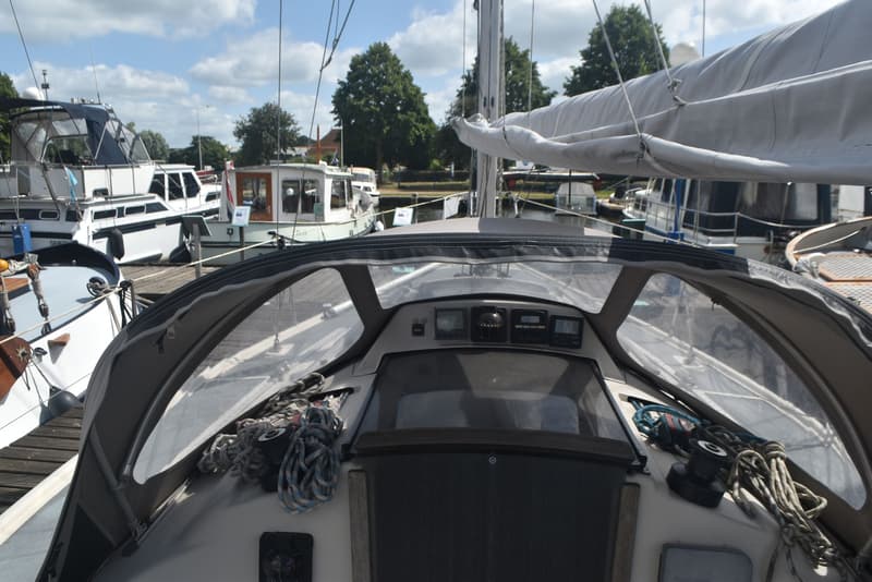 Een bovenaanzicht van een zeilboot met een cockpitkap, instrumentenpaneel en opgerolde zeilen, omringd door andere boten in…