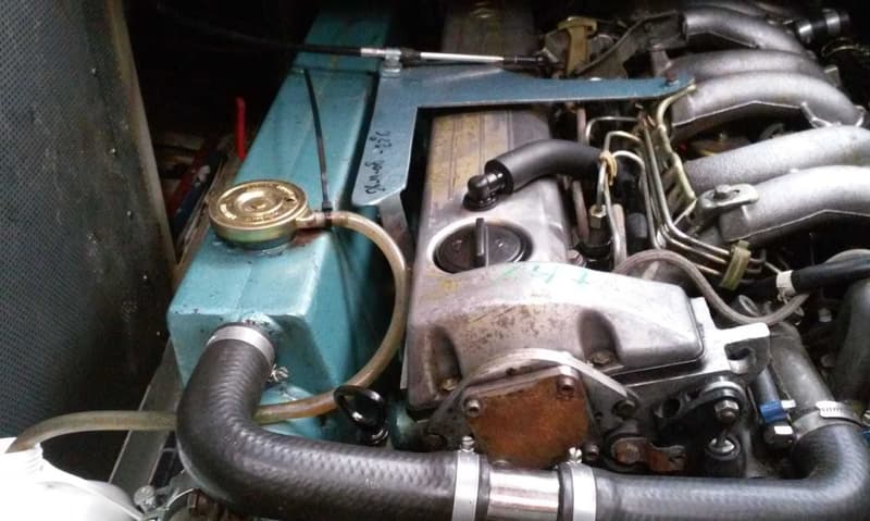 Een close-up van een scheepsmotor met diverse slangen, leidingen en een blauw geverfd onderdeel.