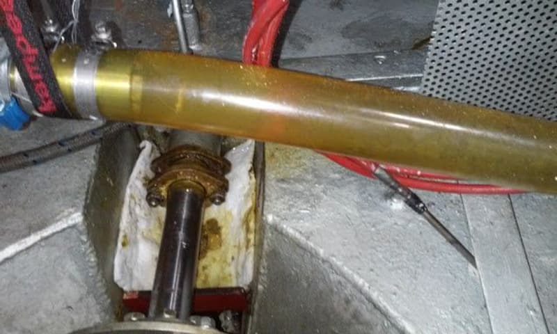 Een detailfoto van een scheepsonderdeel met een doorzichtige buis, een as en een witte doek met bruine vlekken.