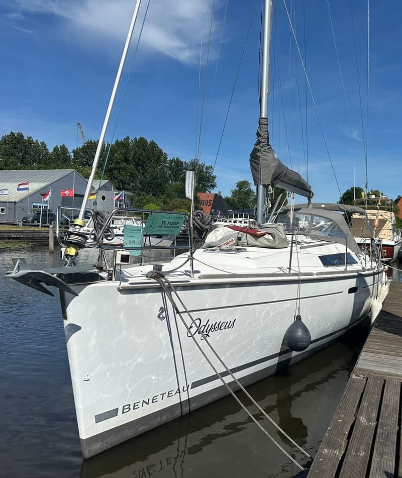 Een witte zeilboot met de naam "Odysseus" en "BENETEAU" op de romp ligt aangemeerd aan een houten steiger.