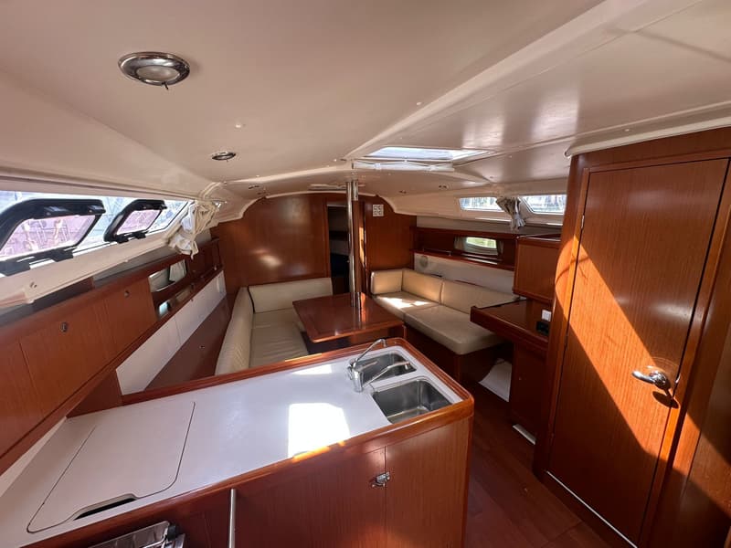 De foto toont het interieur van een boot met een kombuis, zithoek, houten meubels en ramen. — Beneteau Oceanis 37