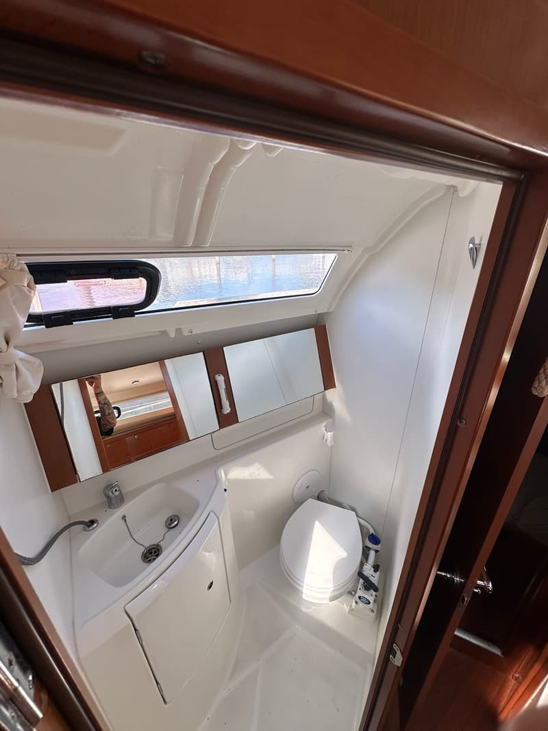 De foto toont een badkamer met een toilet, wastafel, spiegelkast en een raam met uitzicht op water.