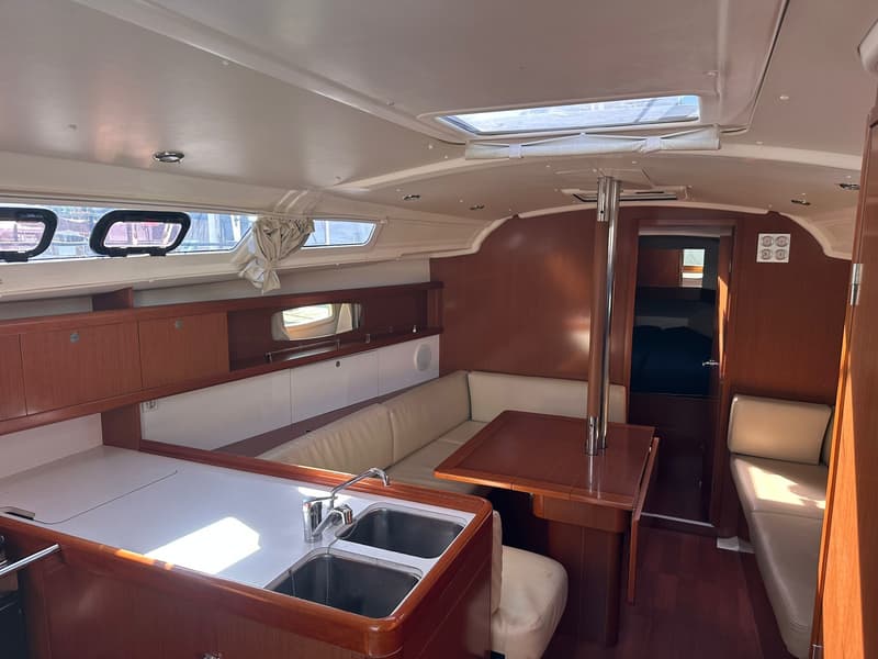 De foto toont het interieur van een boot met een kombuis, zithoek met tafel en een doorgang naar een hut.