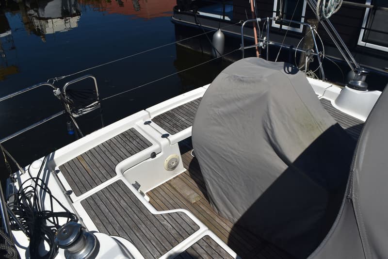 Een dek van een zeilboot met teakhouten planken, een grijze afdekhoes en een luidspreker. — Beneteau Oceanis 37
