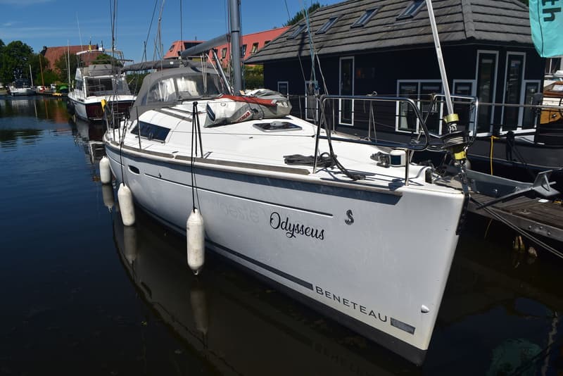 Een witte zeilboot met de naam "Odysseus" en "BENETEAU" op de romp ligt aangemeerd in een haven. — Beneteau Oceanis 37