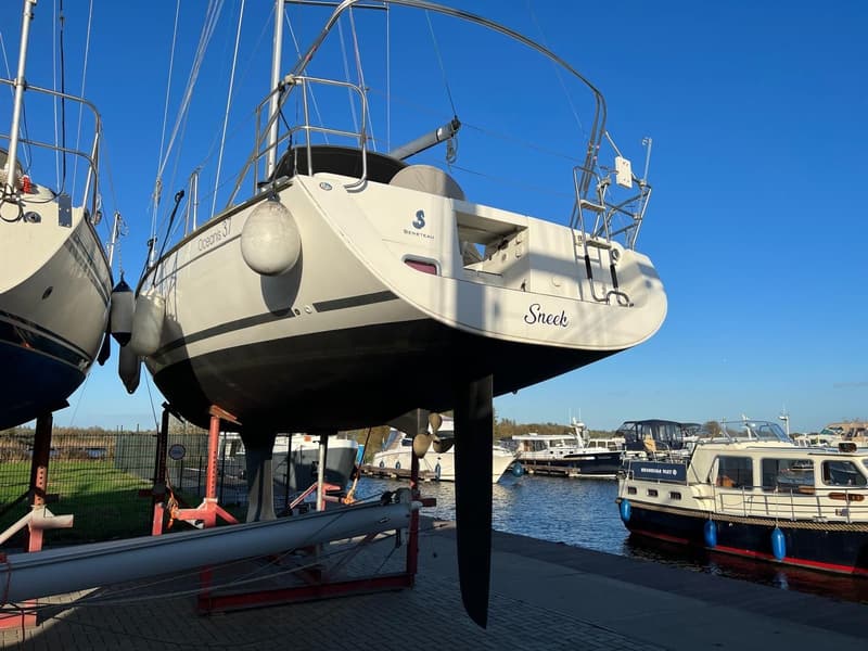 Een witte zeilboot met de naam "Sneek" en "Oceanis 37" staat op de wal naast een andere boot. — Beneteau Oceanis 37