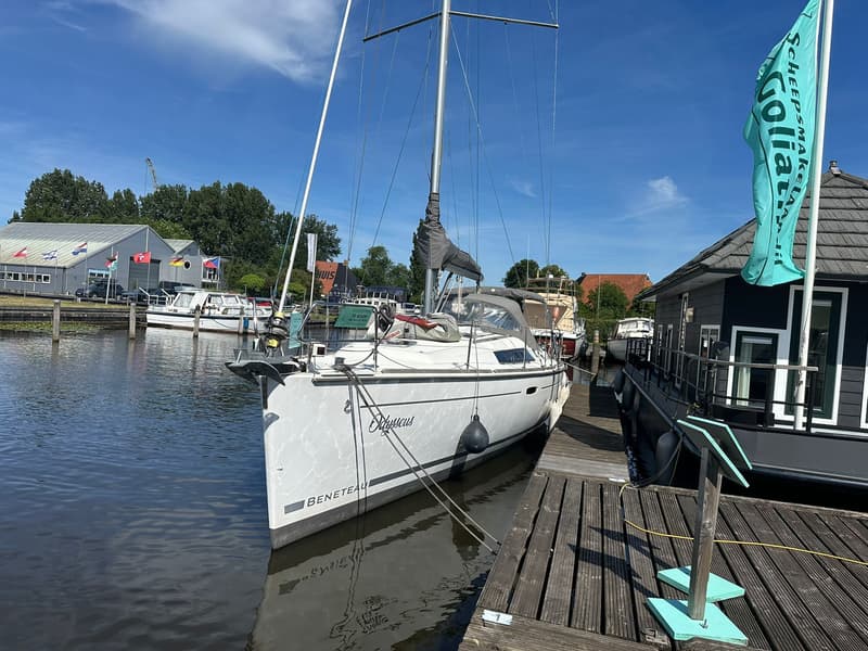 Een witte zeilboot met de naam "Odysseus" en "BENETEAU" op de romp ligt aangemeerd aan een houten steiger.