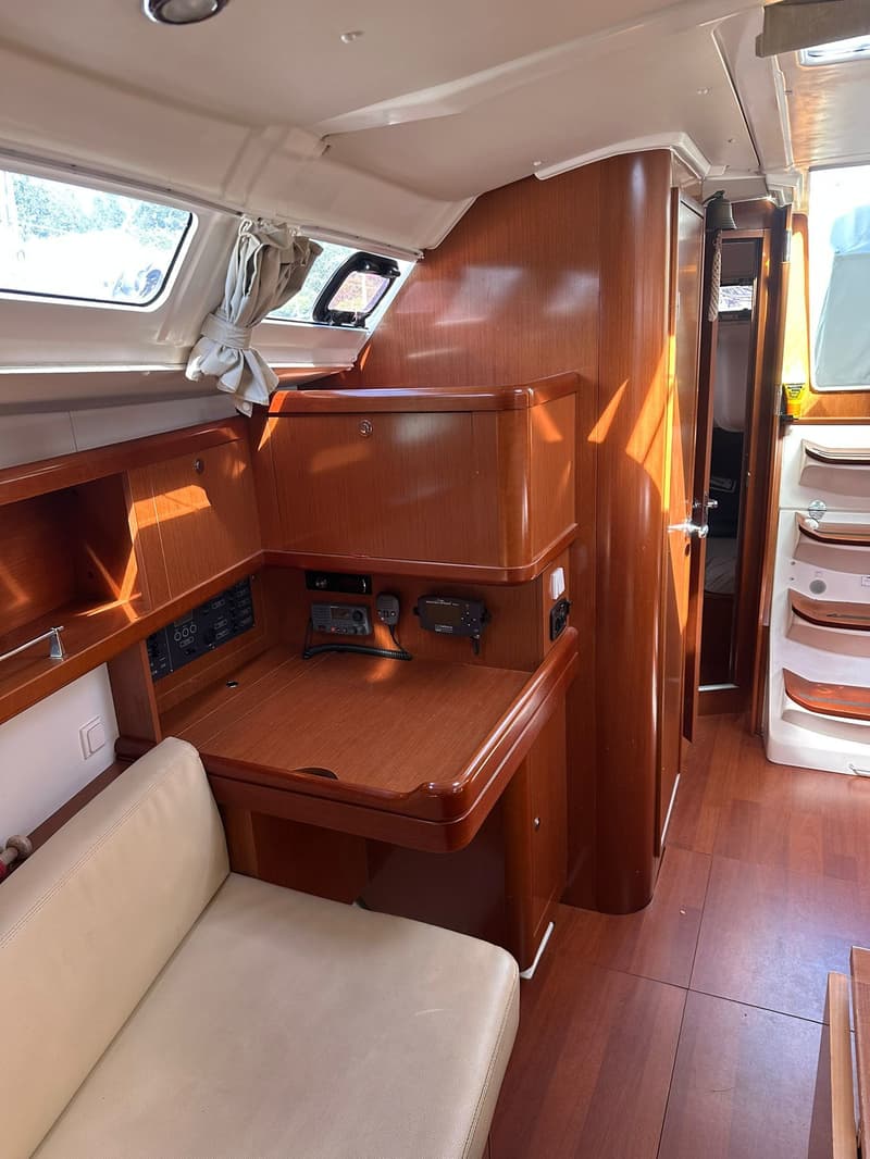 De foto toont het interieur van een boot met houten meubilair, een beige bank, ramen en een trap. — Beneteau Oceanis 37