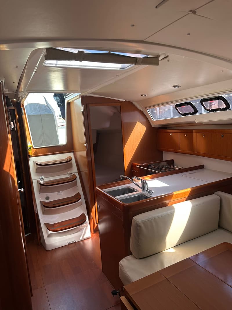 De foto toont het interieur van een boot met een kombuis, zithoek, houten vloer en een trap naar het dek.