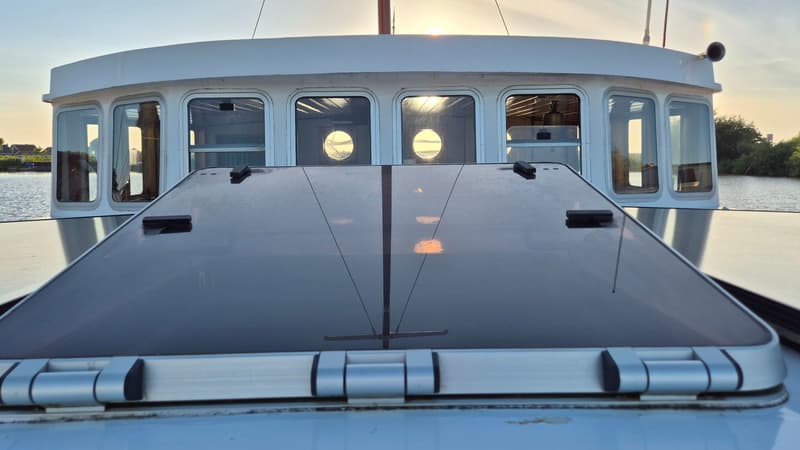 De foto toont de achterkant van een witte boot met een glazen dak en ramen, varend op water bij zonsondergang. — Botter 14.99