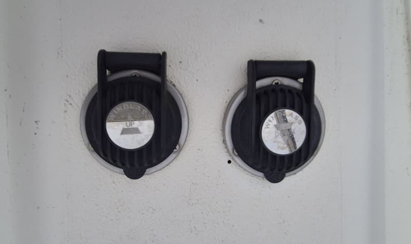 Twee ronde, zwarte bedieningspanelen met zilverkleurige randen zijn gemonteerd op een lichtgrijze ondergrond.