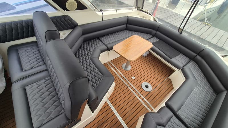 De foto toont een bootinterieur met een U-vormige zwarte bank, een houten tafel en een houten vloer.