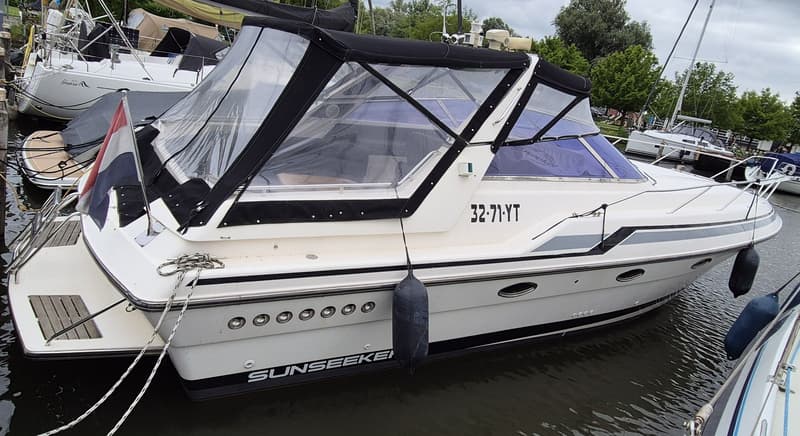 Een witte motorboot met een zwarte kap en een Nederlands vlaggetje ligt aangemeerd in een haven. — Sunseeker 38 Martinique