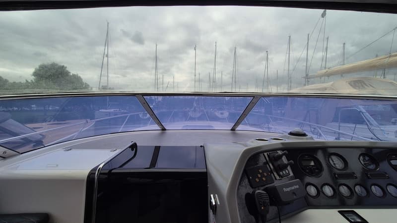 Een interieurfoto van een boot met een stuurconsole, een Raymarine marifoon en een voorruit met uitzicht op zeilboten in…