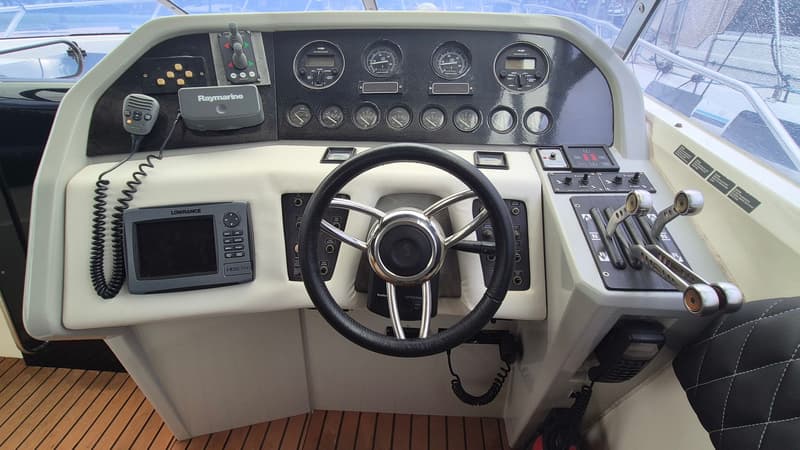 De foto toont het dashboard van een boot met een stuurwiel, diverse meters, een Lowrance HDS7m en een Raymarine apparaat.