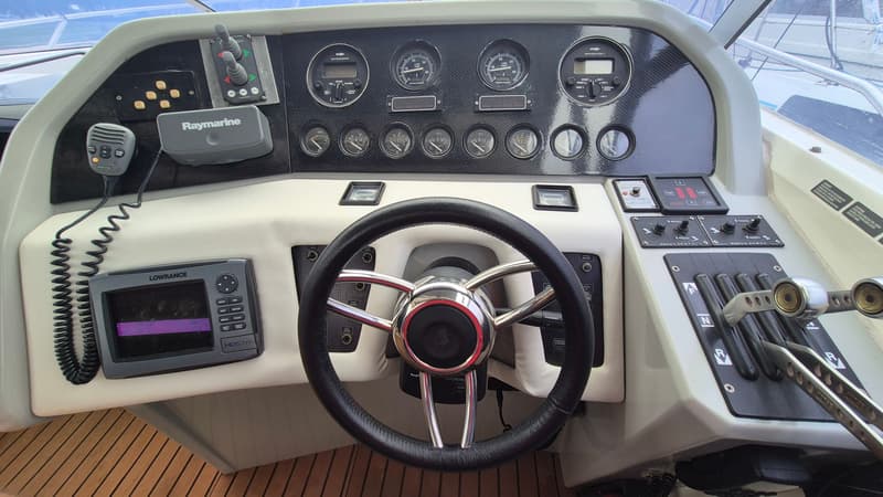 Een stuurstand van een boot met een zwart stuur, diverse meters, een Lowrance HDS7m en een Raymarine marifoon.