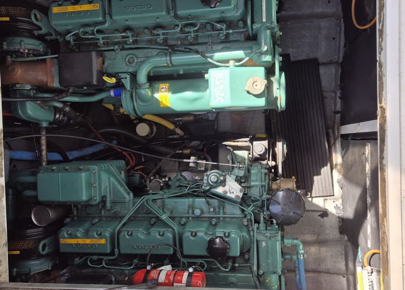 Twee groene Volvo Penta motoren met diverse slangen, kabels en een brandblusser in een motorruimte.