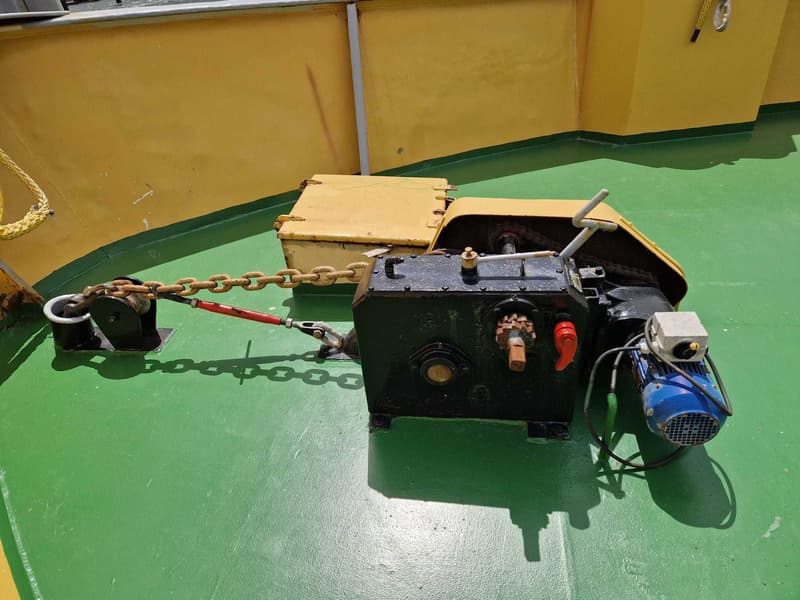 Een ankerlier met ketting en een blauwe elektromotor op een groen dek met een gele romp.