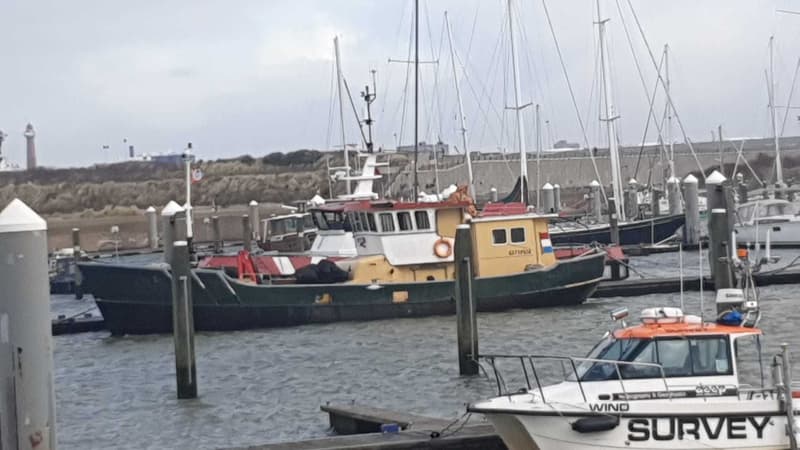 Een groene, gele en witte boot met een rood-wit gestreepte boeg ligt afgemeerd in een haven.