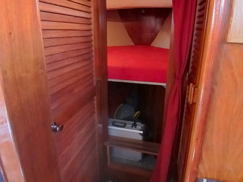 Een houten interieur met een rood bed en een rode gordijn, met een koffer en een plank eronder.