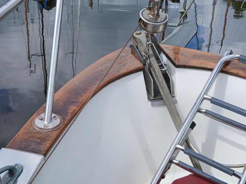 De boeg van een witte boot met een houten rand, een ankerlier en een metalen zwemtrap is zichtbaar. — Fisher 34