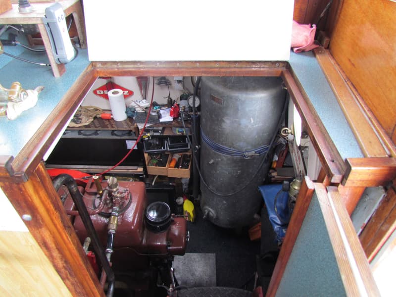 Een blik in de motorruimte van een boot, met een roodbruine motor en een grote grijze tank.