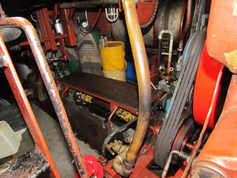 Een close-up van een scheepsmotorruimte met diverse machines, riemen, slangen en een gele emmer.