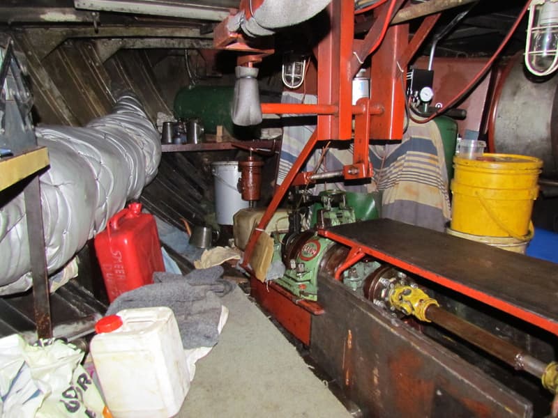 De foto toont een rommelige machinekamer met een motor, diverse jerrycans, emmers en leidingen.