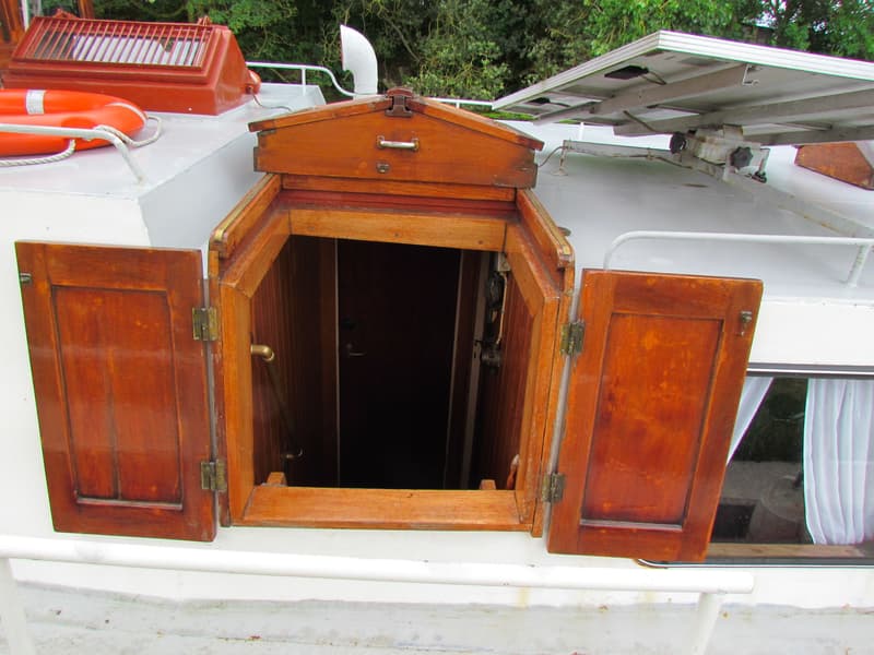 Een open houten kajuitingang met twee deuren en een luik, met een reddingsboei en zonnepanelen op het dek.