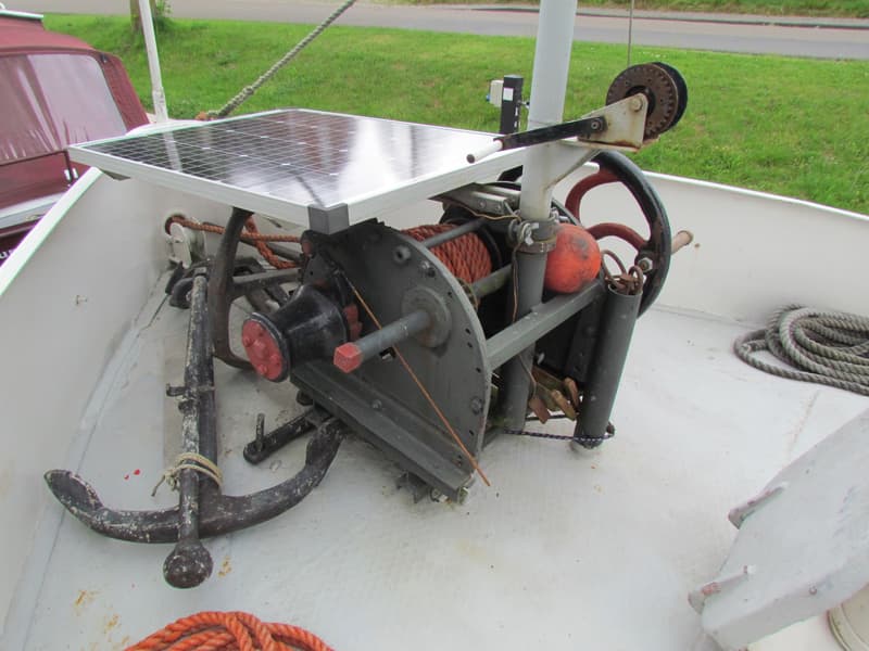 Een ankerlier met een zonnepaneel erboven, een anker en touwen op het dek van een boot. — Hamburger Schuit Varend Woonschip